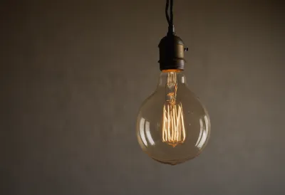A single bare filament bulb hanging on a cord in a dark, empty room, its coiled filament glowing a low amber rather than bright white.