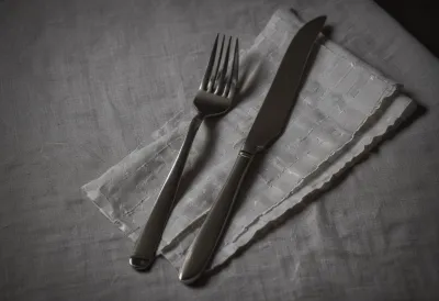 A single stainless steel dinner fork resting on a folded linen napkin.