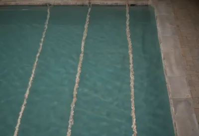 Overhead view of an empty floodlit swimming pool at night, its still surface divided into parallel stripes by lane ropes.