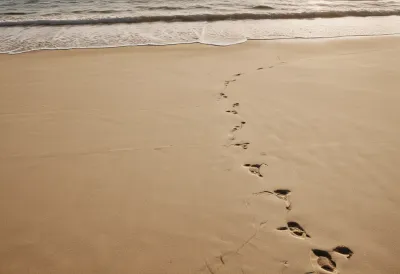 A long line of footprints crossing wet, reflective sand toward the horizon on an empty beach under a low sun