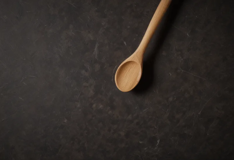 A plain wooden spoon lying on a kitchen counter, seen from above.