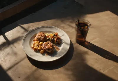 A single plate of food on a dark table, half in shadow and half lit by a warm pool of window light, seen from above