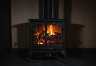A cast-iron stove door standing open in a cold dark room at night, the embers inside glowing fierce orange