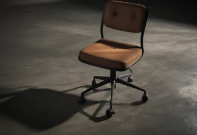 An empty office chair standing alone on a wide expanse of bare concrete floor, its seat cushion still holding a deep dent.