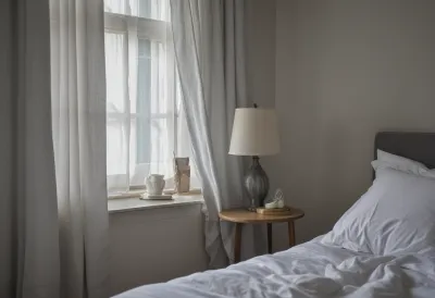 Rumpled white bedsheets and an empty bedside table in the thin grey light of early morning coming through a gap in the curtains.