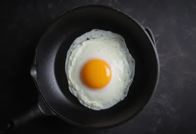 A single egg frying in a pan, the translucent white turning opaque and setting at the edges, seen from above