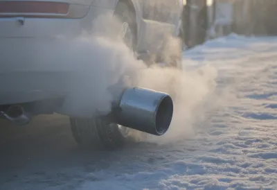 A thick plume of white exhaust vapour curling from a car tailpipe into freezing morning air