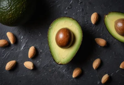A halved ripe avocado with golden olive oil pooled in its hollow and a few almonds scattered beside it.