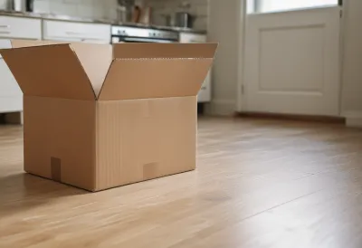 A half-unpacked cardboard moving box standing on the floor of an otherwise empty kitchen in bare morning light.