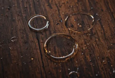 Overlapping wet rings on a dark polished bar top beside an uncorked bottle in low amber light
