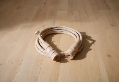 A coiled jump rope with wooden handles lying on a pale wooden floor.