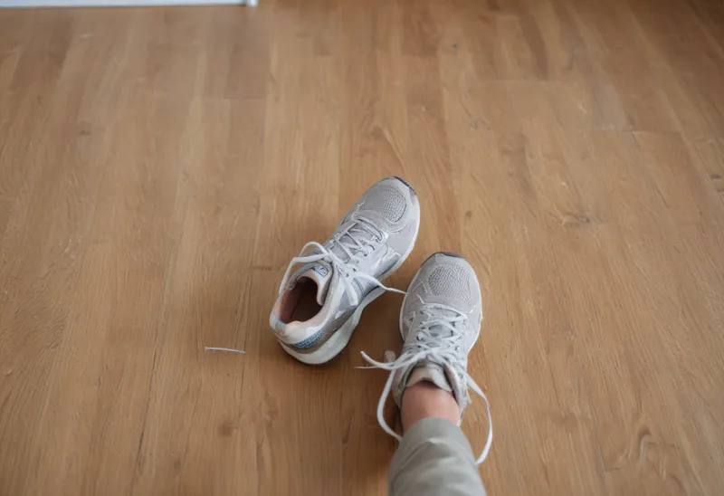 A pair of running shoes sitting on a wooden bedroom floor.