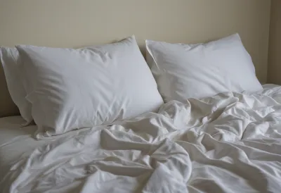 An empty bed at dawn with the sheets thrown back and a deep hollow pressed into the pillow