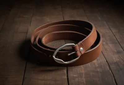 A coiled brown leather belt on a bare wooden surface.