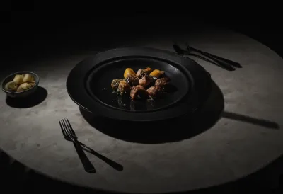 A half-eaten plate of dinner lit by a hard circular pool of overhead light, with the surrounding table in darkness