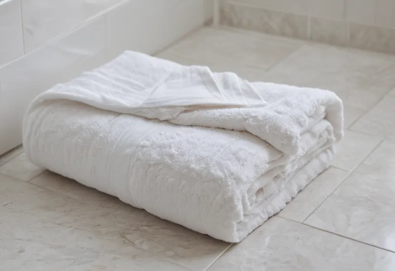 A folded white bath towel resting on a bathroom floor.