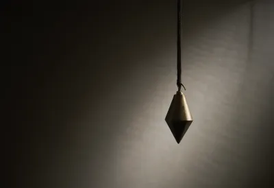 A single brass plumb bob hanging motionless and centered on a thin cord, lit by one hard shaft of light against deep shadow