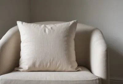 A plump pale linen cushion resting on a light armchair in a quiet room.